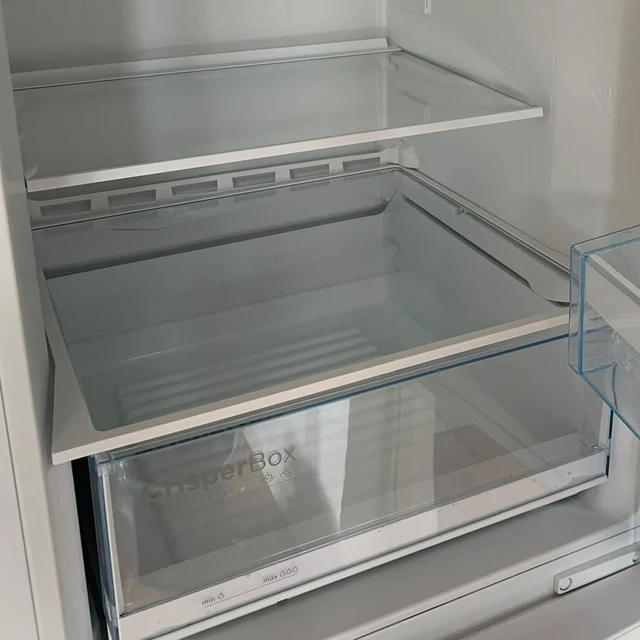 Samma kylskåp efter flyttstädningen, med ren glashylla och grönsakslåda