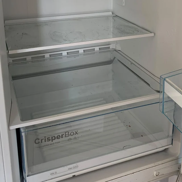 Kylskåpet före flyttstädningen, med fläckar och rester på glashyllan och i grönsakslådan