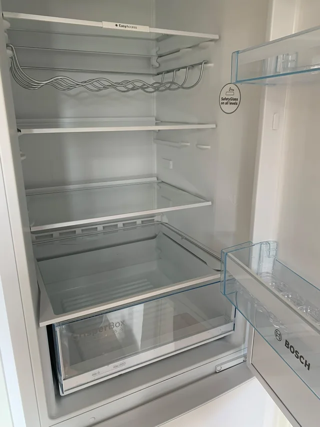 Tomt kylskåp med glashyllor och grönsakslåda efter flyttstädningen