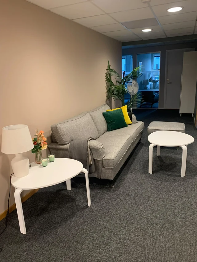 Soffhörna med grå soffa, bordslampa och blommor på Novelias kontor